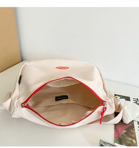 Detail view of the spacious inner compartment and red zipper of the cream nylon bag