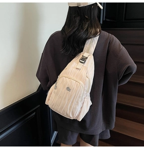 Detail of light beige pleated crossbody bag featuring durable zippers and a secure buckle