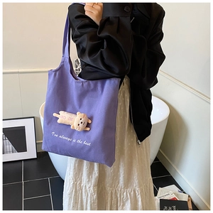 Detail of purple canvas tote bag featuring a 3D plush bear and artistic text slogan