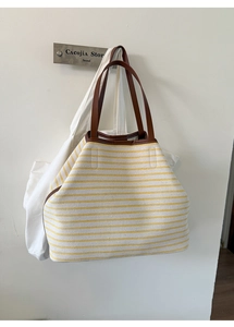 Detail view of the yellow striped tote bag featuring premium brown leather handles and stitching