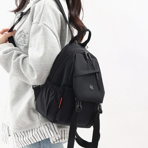 Close-up of black oxford backpack with dual front zippers and round metal logo detail