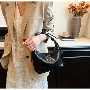 Close-up of black leather half-moon shoulder bag with fine stitching and slim strap