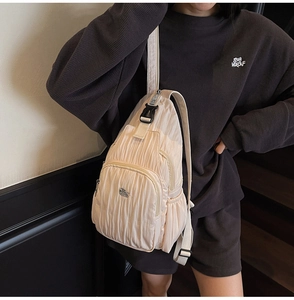 Detail showing creamy pleated fabric texture and zipper pocket on a versatile sling bag