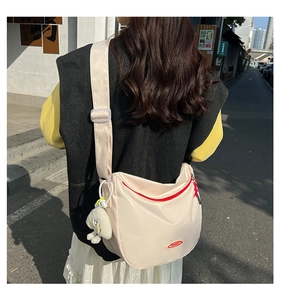 Detail of beige nylon crescent bag with red zipper and plush charm accessory