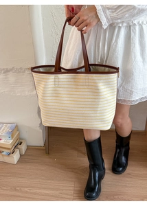 Detail of yellow striped tote bag featuring premium dark brown leather handles and canvas texture