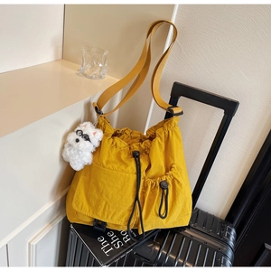 Bright yellow drawstring crossbody bucket bag with cute plush puppy charm on a suitcase
