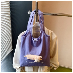 Detail of purple canvas tote bag featuring a 3D plush cat doll and printed lettering