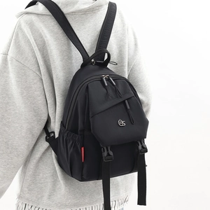 Detail of a black nylon waterproof backpack with metal logo and side water bottle pockets