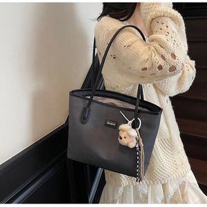 Detail of grey tote bag with wavy texture and white bow bear charm on wooden stairs