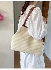 Detail of yellow striped canvas tote bag showing brown leather straps and fine stitching