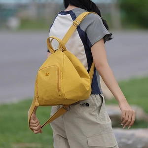 Detail of a mustard yellow triangle nylon backpack with embroidered logo and sleek texture