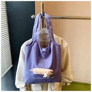 Detail of purple canvas tote bag featuring a 3D plush cat doll and white embroidery