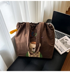 Detail of brown canvas tote bag with bear embroidery and yellow strap on a bench
