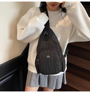 Detail of black vertical pleated crossbody bag with silver metal logo and buckle
