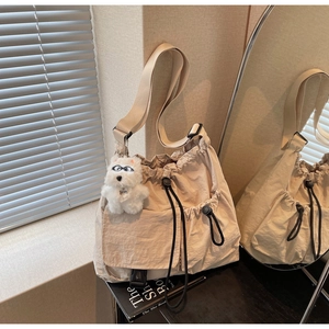 Detailed close-up of beige nylon drawstring bucket bag with buckle pocket and plush charm