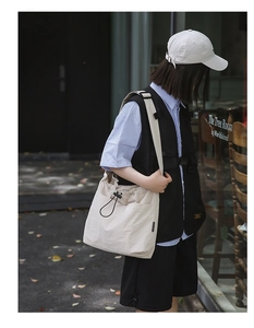Detail of off-white nylon drawstring bucket bag with black cords on a street style model