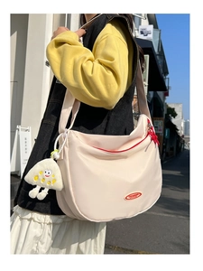 Detail of cream nylon crescent crossbody bag with red zipper and plush monster charm