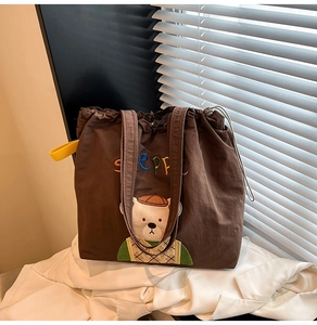 Detail of cute bear embroidery and drawstring closure on a brown canvas tote bag