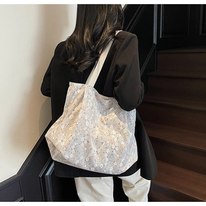 Detail of white lace tote bag with blue and orange floral embroidery on a shoulder strap