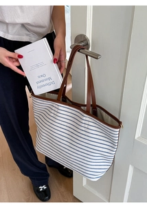 Spacious striped canvas tote bag with brown leather handles hanging on a door handle