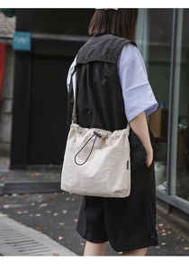 Outdoor lifestyle shot of a cream nylon drawstring bucket bag with pleated details
