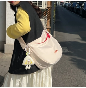 Detailed close-up of off-white nylon crossbody bag with red logo and plush charm
