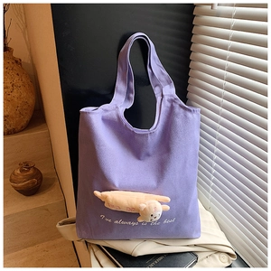 Detail of purple canvas tote bag featuring a cute plush doll and embroidered lettering