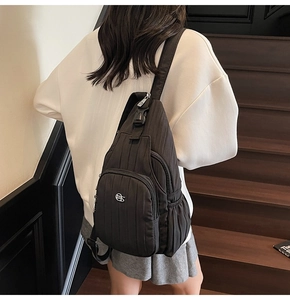 Detail of the black pleated fabric texture and silver metal logo on a crossbody bag