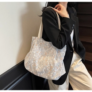 Detail view of light blue floral lace tote bag with canvas straps worn by a model