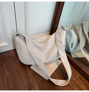 Detail einer beigen Canvas Hobo-Tasche mit breitem Gurt und Logo auf weißem Hintergrund