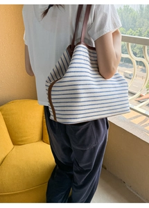 Detail of striped canvas tote bag with brown leather trim and shoulder strap view