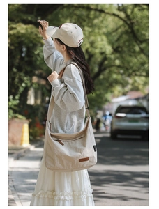 Detail of beige crescent canvas crossbody bag with wide strap and brown leather patch
