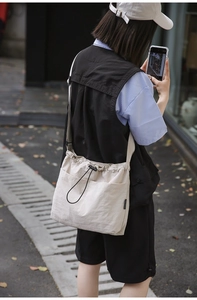 Detail of cream nylon drawstring crossbody bag with textured pleats and brand tag