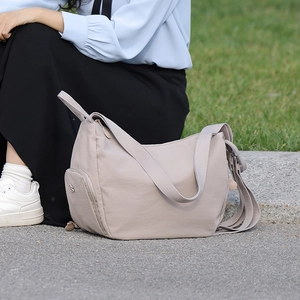 Detail of light brown nylon backpack with side zipper pocket and metal logo accent