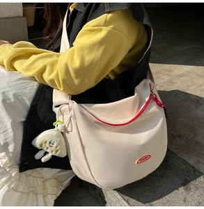 Close-up of off-white nylon crossbody bag with red zipper and plush charm on wide strap