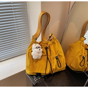 Detail of yellow nylon drawstring bucket bag with plush puppy charm and adjustable strap