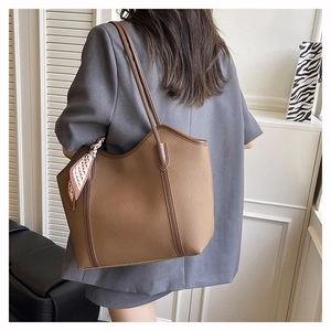 Brown leather tote bag with silk scarf on shoulder of model wearing a grey blazer