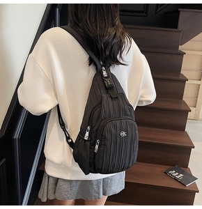 Detail of black pleated nylon crossbody bag featuring dual silver zippers and adjustable strap
