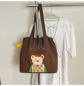 Close-up of brown tote bag featuring cute bear embroidery and yellow drawstring details
