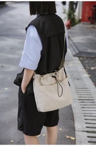 Detail of a beige nylon bucket bag with drawstring closure and large front utility pockets