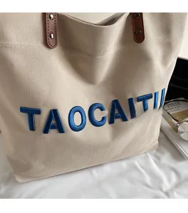 Close-up of beige canvas tote bag with blue 3D embroidery and brown leather handle rivets