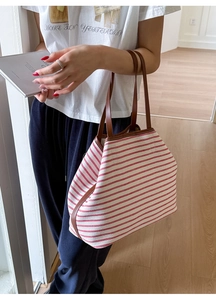 Detail of red striped canvas tote bag with brown leather straps held by a model