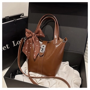 Dettaglio di una borsa a secchiello marrone lucido con foulard e chiusura a girello argento