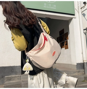 Beige nylon crescent crossbody bag with red zipper and plush charm shown on model
