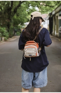 Outdoor view of an orange and beige crossbody bag with elastic drawstrings and mesh pocket