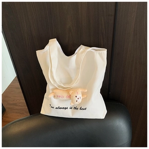 Detail of white canvas tote bag featuring a cute cat plush charm and printed typography