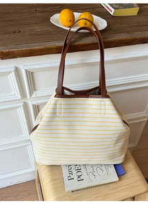 Detail of yellow striped canvas tote bag with brown leather handles on wooden stool