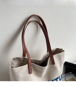 Close-up of canvas tote bag showing brown leather straps and blue side lettering