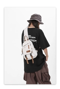 Detail of white canvas crossbody bag with brown leather trim and plastic buckle closure