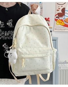 Close-up of cream canvas backpack featuring green star prints and a plush bear charm